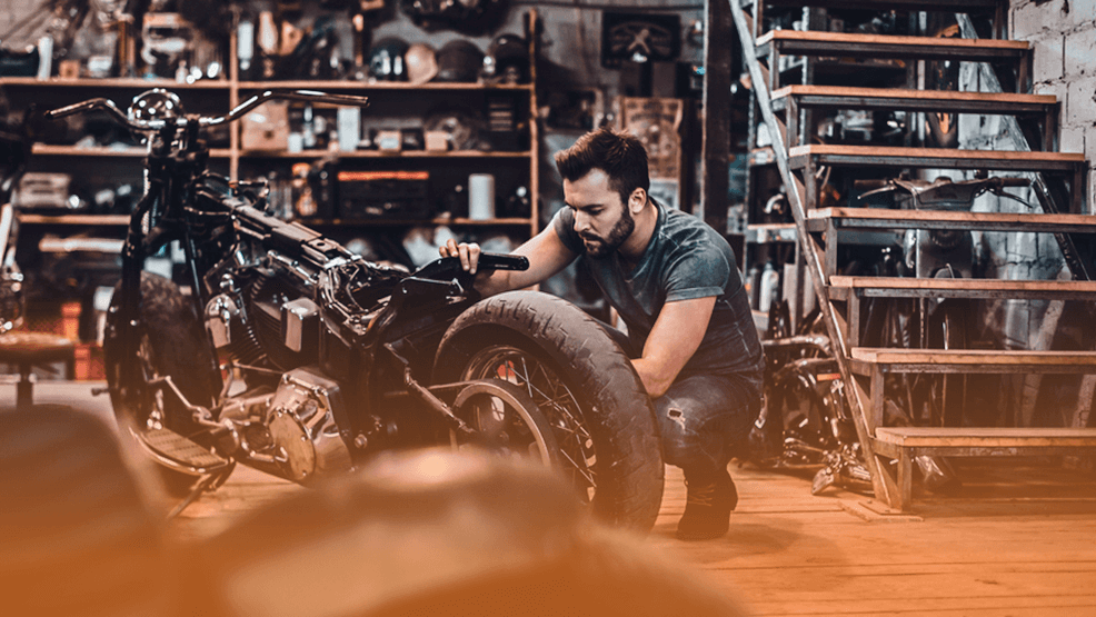 Motero con barba en taller con moto