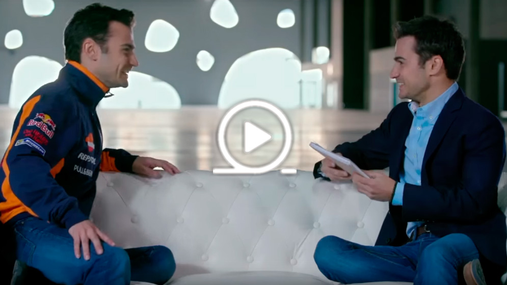 Dani Pedrosa consigo mismo en sofá blanco e icono de play