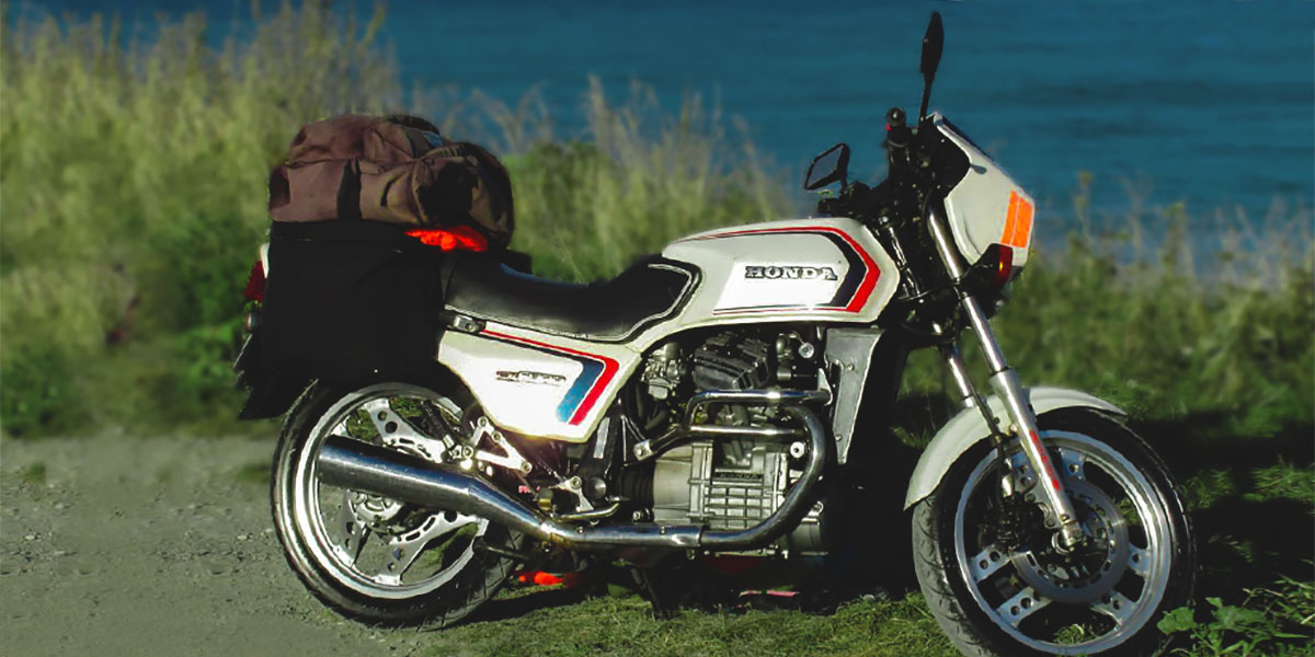 Honda CX 500 aparcada en la vegetación frente a un lago muestra las llantas comstar