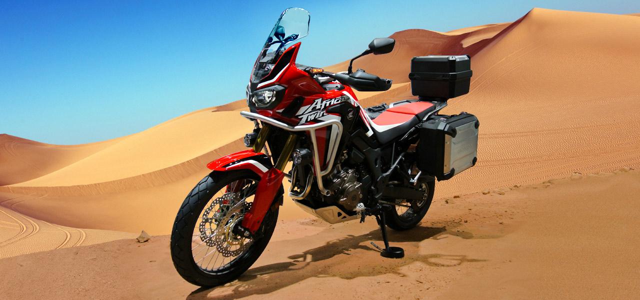 Una Honda Africa Twin de lado con dunas dunas de fondo en el desierto