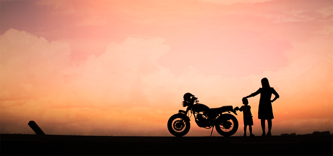 una moto de perfil vista sobre el ocaso con una motera y su hijo alrededor