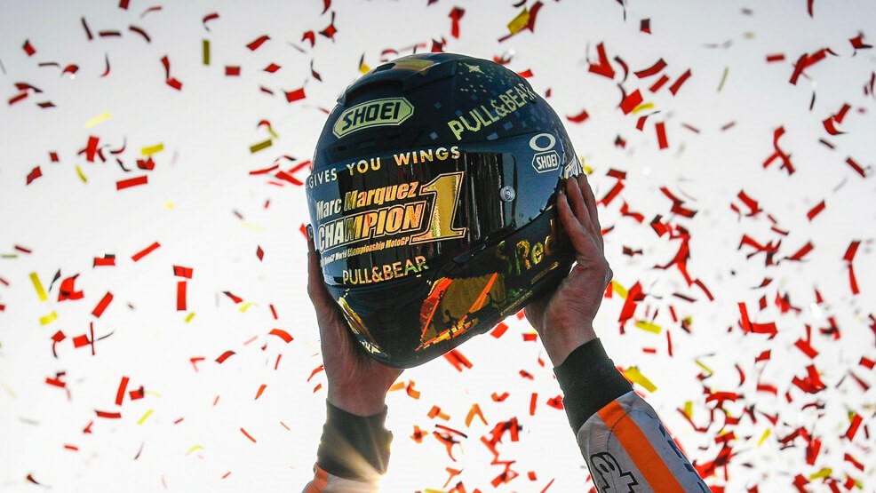 Las manos de marc levantan el casco de campeón rodeado de confetti naranja y rojo
