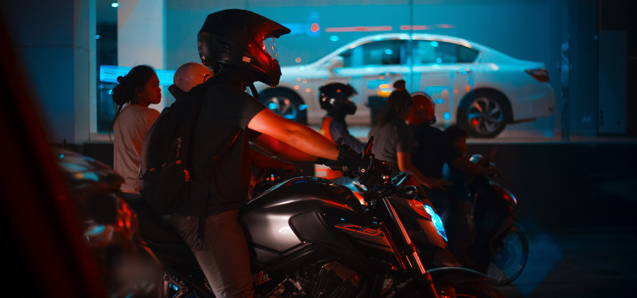 Motorista de perfil circula en su moto de noche con un escaparate detrás de él