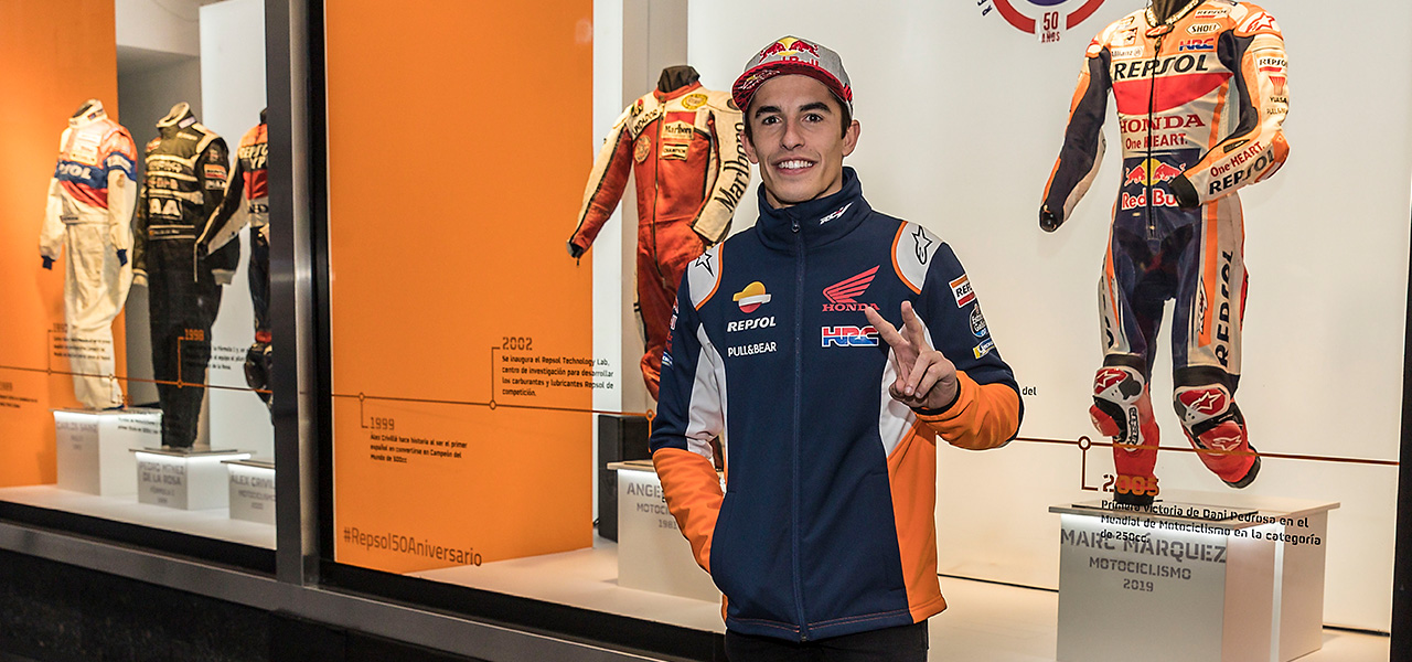 Marc Márquez haciendo el saludo en V en exposición de monos de competición.