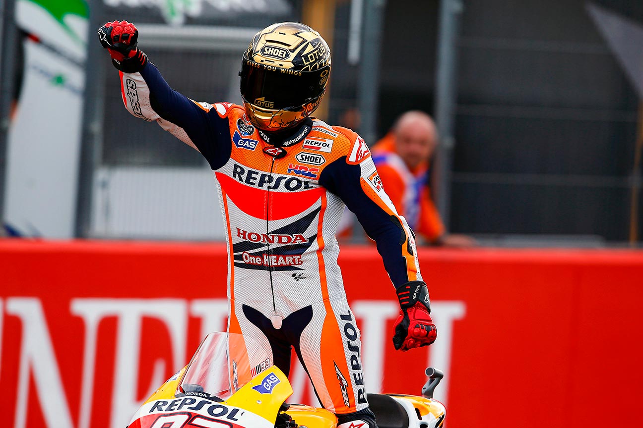 Marc Márquez con casco dorado levantado sobre la moto