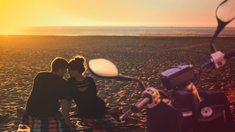 Pareja sentada en la playa con moto